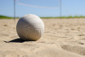 A volleyball rests on a sunny beach with a clear blue sky in the background, much like the inviting atmosphere of Spare Time Texas. The sand is smooth, and a blurred net can be seen in the distance, reminiscent of the lanes at this family fun center where bowling brings loved ones together.