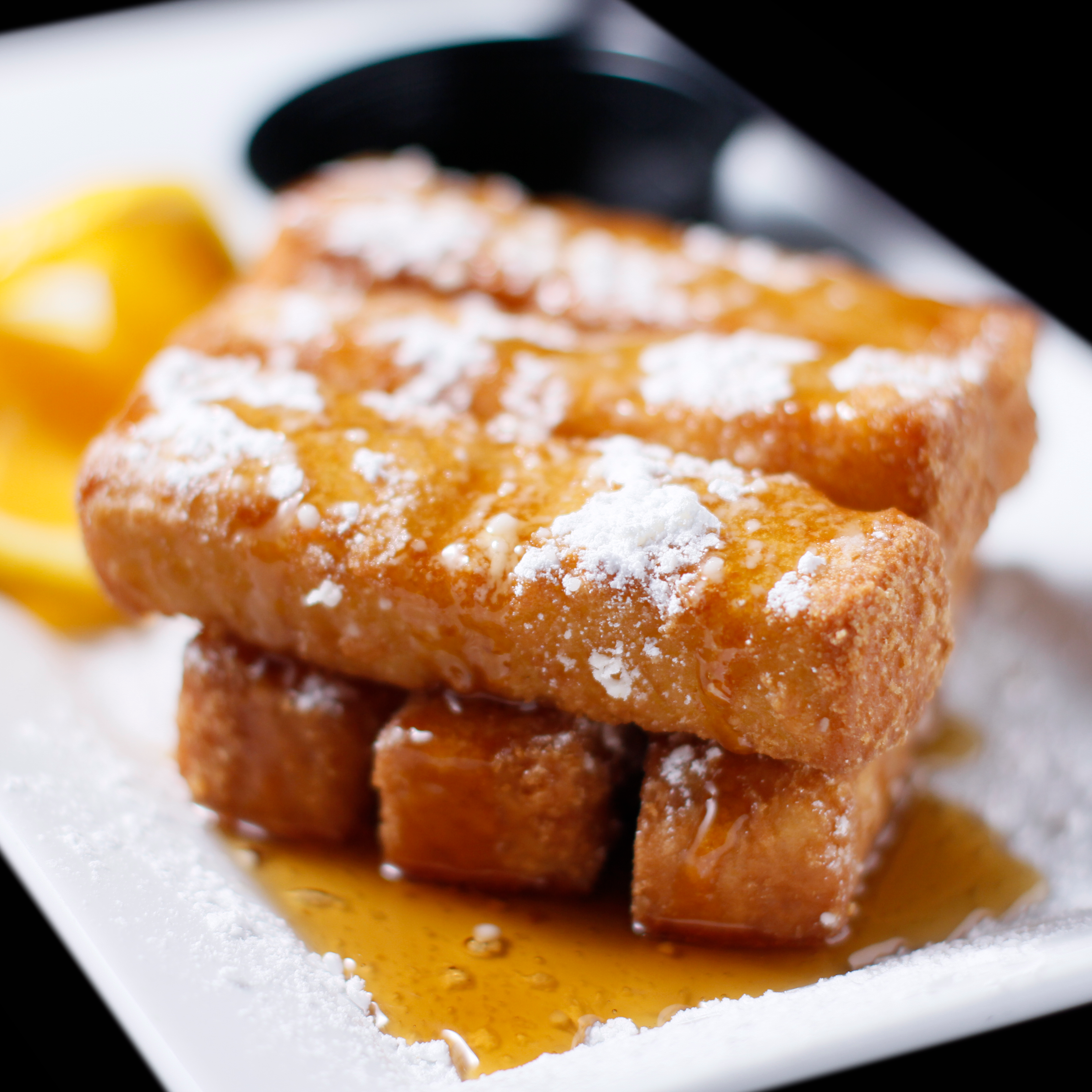 At Spare Time Texas, start your day with a stacked serving of French toast topped with powdered sugar and syrup, all on a white plate. Perfect for indulging in some sweet family fun at the center before heading to the bowling lanes. Don't forget the lemon slice in the background!.