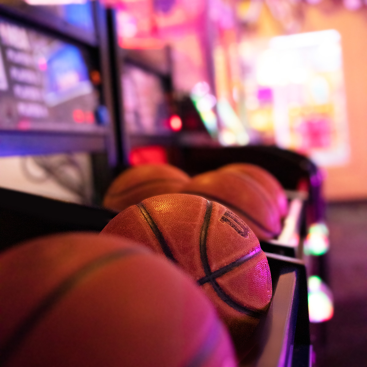 Close-up of basketballs arranged in rows at an arcade game in Spare Time Texas. The background is softly blurred, showcasing colorful lights and arcade machines, creating a lively and vibrant atmosphere perfect for a family fun center experience.