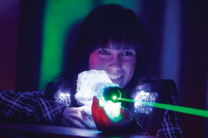 Amidst the glowing ambiance and futuristic vibe at Spare Time Texas, a person beams with excitement while playing laser tag, aiming a laser gun with a glowing green beam. The dim setting enhances this thrilling family fun center experience, where adventure meets play in every corner.
