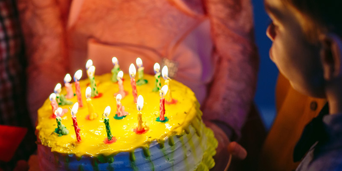 A child gazes at a brightly lit birthday cake adorned with colorful candles, set in the lively Spare Time Texas family fun center. The yellow icing and vibrant sprinkles add to the festive mood, while a person in a pink outfit likely holds the cake amidst the joyful chaos of bowling games.