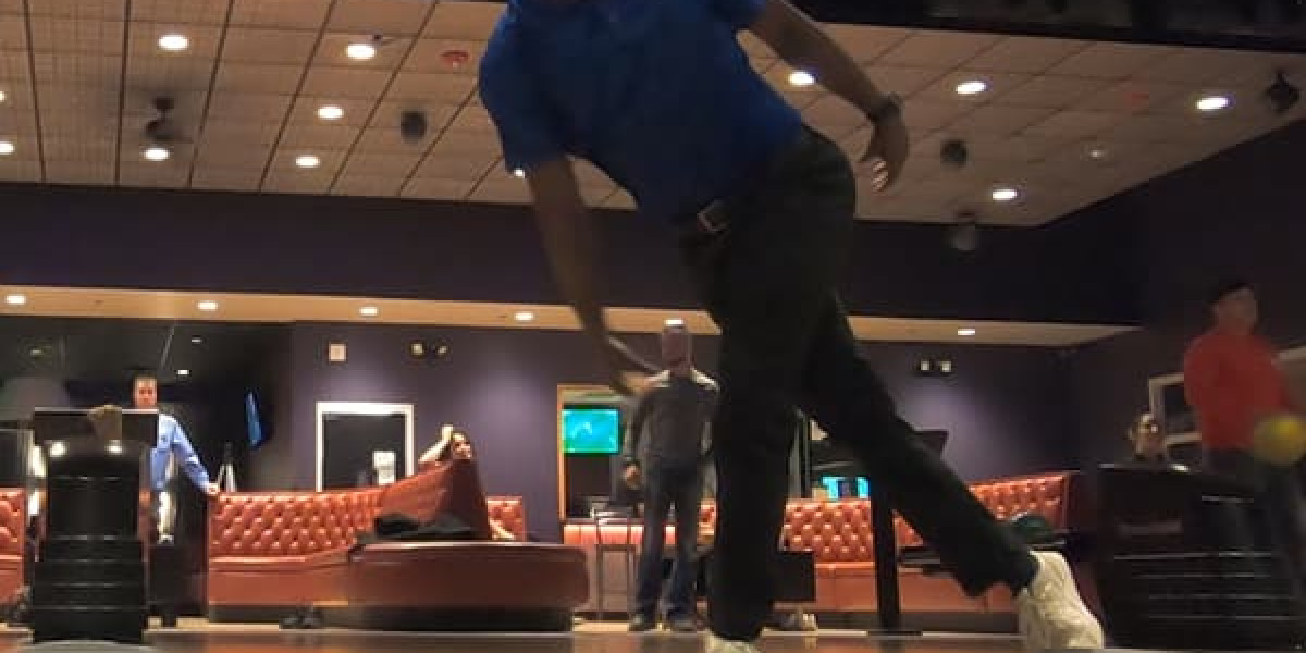 A person in a blue shirt is bowling mid-throw at Spare Time Texas, where the lively atmosphere captures the essence of a family fun center. In the background, people relax on red couches under a well-lit, tiled ceiling.