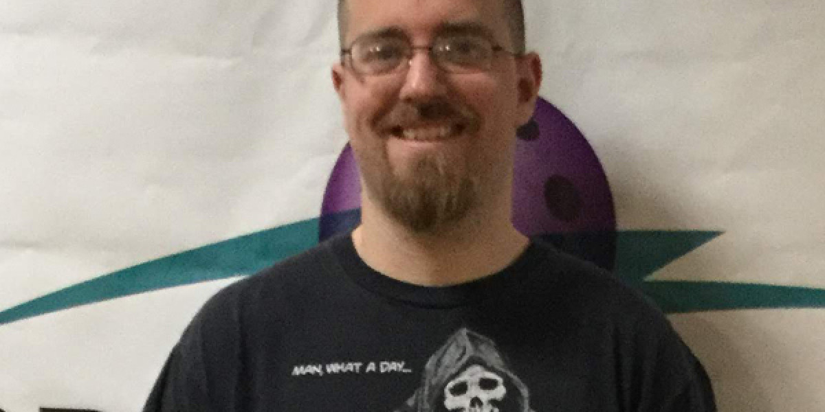 A person with glasses and a goatee is smiling, wearing a T-shirt featuring a skull design and the phrase "MAN, WHAT A DAY..." They stand in front of a banner with a partial logo at Spare Time Texas, perhaps reminiscing about an exciting bowling session at the family fun center.