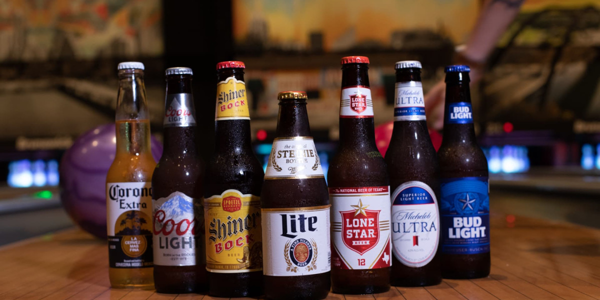 A row of various beer bottles, including Corona Extra, Coors Light, Shiner Bock, Miller Lite, Lone Star, Michelob Ultra, and Bud Light, is displayed on a wooden surface at Spare Time Texas. The colorful, blurred background evokes the vibrant atmosphere of a family fun center complete with bowling excitement.
