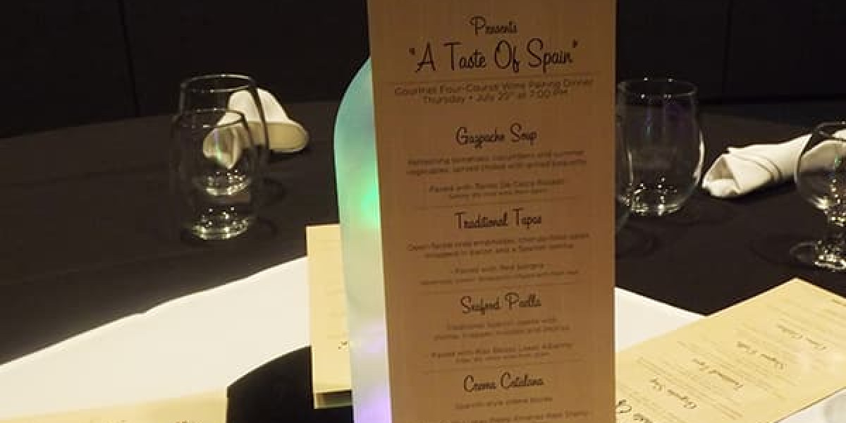 A close-up of a restaurant menu titled "A Taste of Spain" at Spare Time Texas. The menu features Gazpacho Soup, Traditional Tapas, Seafood Paella, and Crema Catalana. It's displayed on a table with glassware and napkins in the background, adding a touch of elegance to this family fun center.