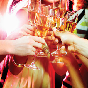 A group of people clinking glasses filled with champagne, celebrating at a lively event in Spare Time Texas. The festive atmosphere of this family fun center is enhanced by vibrant, colorful lights, making the occasion unforgettable.