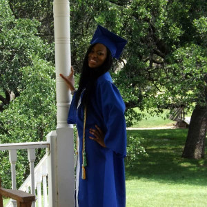 A person in a blue graduation gown and cap stands on a porch, smiling and posing with one hand on a column. Surrounded by lush green trees in the background, they recall the family fun times spent at Spare Time Texas, where bowling was always a cherished pastime.
.