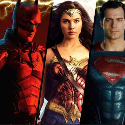 Three superhero figures strike dynamic poses: one in a red and black bat-themed suit, another in gold and red armor with a star tiara, and the third in a blue suit with a red "S" emblem. Their powerful stances evoke the electrifying energy found at Spare Time Texas, where family fun meets action-packed adventure.