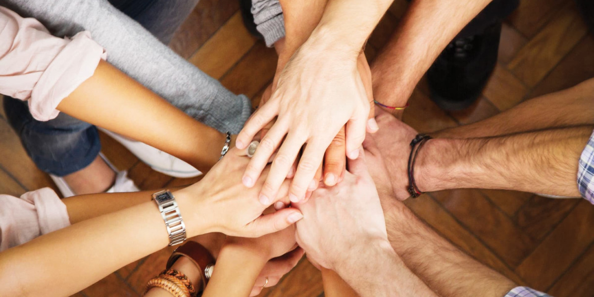 A group of people placing their hands together in the center at a local family fun center, displaying unity and teamwork. The diverse individuals' hands overlap on a wooden surface, symbolizing cooperation and collaboration—an ideal scene for bowling enthusiasts in Spare Time Texas.