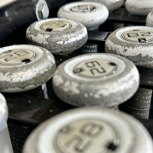 Close-up of worn, textured golf club weights with the number "62" visible on each, reminiscent of the classic gear you'd find at Spare Time Texas. The weights are stacked together, boasting a weathered, grayish appearance, much like the vintage charm sprinkled throughout this family fun center.