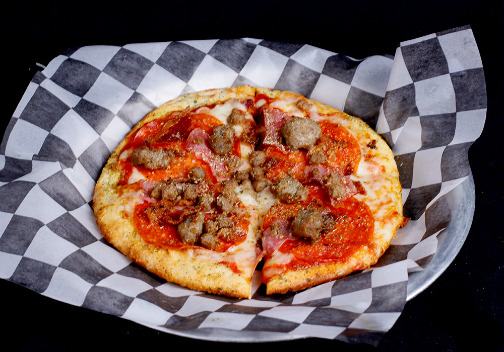 A pizza topped with sausage, pepperoni, and bacon sits on black and white checkered paper on a silver tray, just perfect for a family fun center visit or to enjoy after a few rounds of bowling at Spare Time Texas.