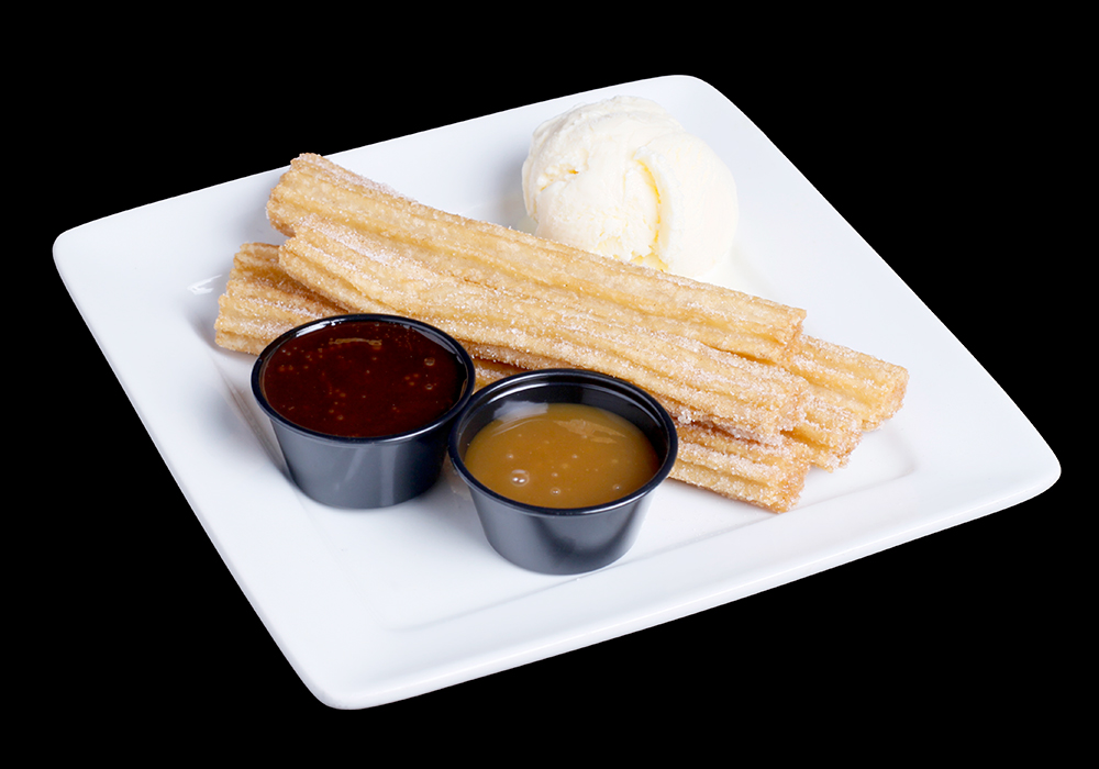 A white plate of churros dusted in sugar, served with vanilla ice cream, awaits you at Spare Time Texas. Two small black cups hold rich chocolate and caramel sauces, enhancing this delightful treat. Perfect for ending a day of bowling or enjoying family fun in this vibrant center.
