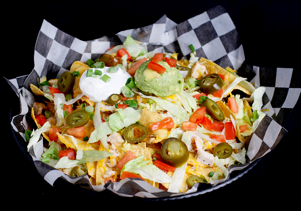 A basket of nachos topped with melted cheese, shredded lettuce, diced tomatoes, jalapeño slices, sour cream, guacamole, and green onions is the perfect snack at Spare Time Texas. Enjoy it at this family fun center where bowling meets delicious bites.