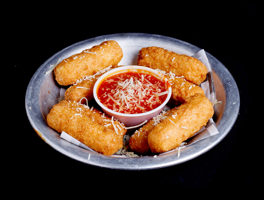 A metal plate showcases six golden-brown, crispy mozzarella sticks surrounding a small bowl of marinara sauce, topped with grated cheese. This tempting snack is perfect for sharing during a family outing at Spare Time Texas, the ultimate family fun center.
