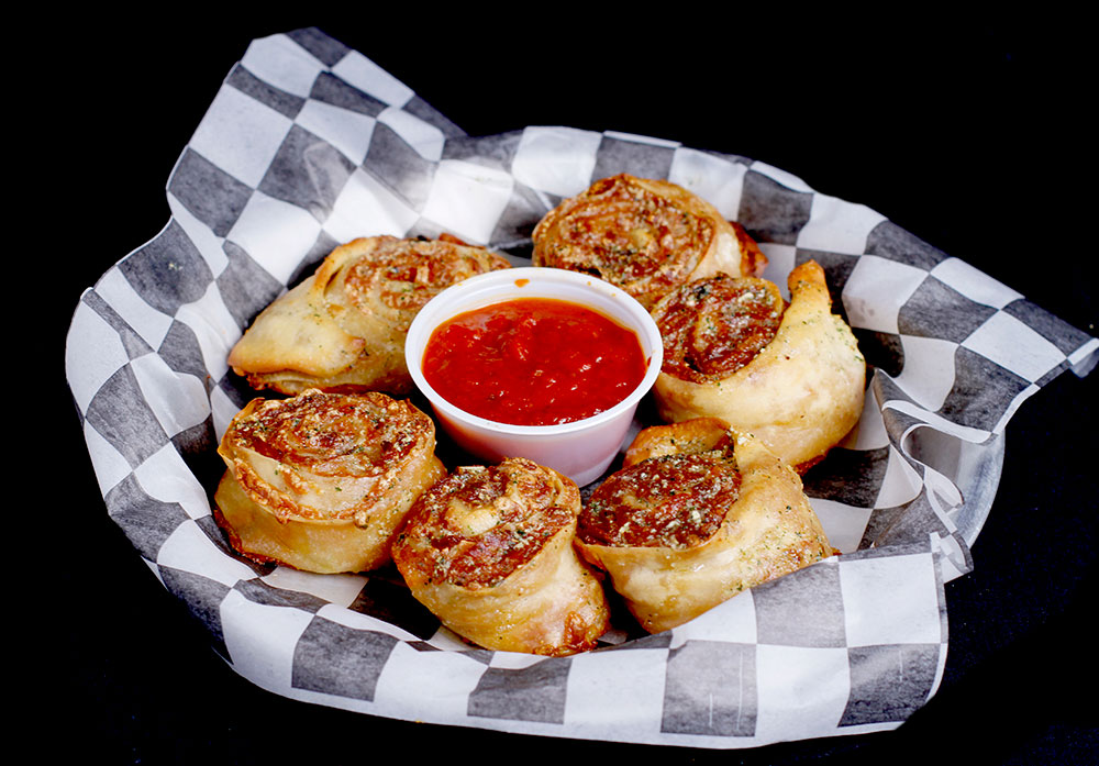 A basket of pizza rolls with a side of marinara sauce, perfect for enjoying at Spare Time Texas. The rolls, arranged on black-and-white checkered paper, boast a golden-brown crust sprinkled with Parmesan cheese, set against a black background—a delicious treat at this family fun center.