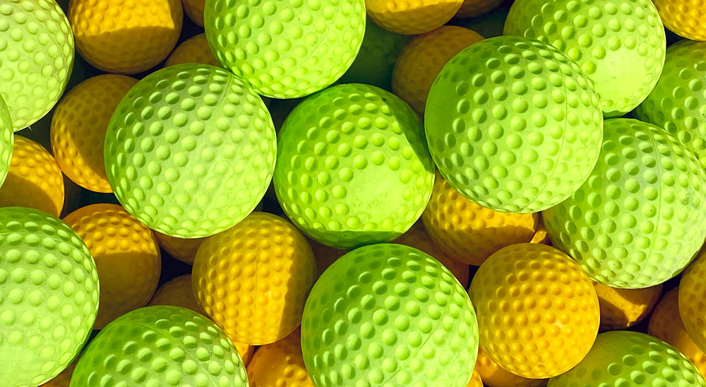 A close-up of numerous textured balls in varying shades of yellow and green captures the essence of Spare Time Texas. Reminiscent of golf balls, their dimpled surfaces, tightly packed, create a playful pattern of light and shadow—perfectly embodying the vibrant energy found at a family fun center.