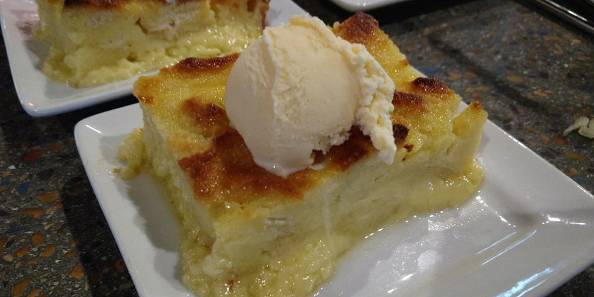 A slice of bread pudding topped with a scoop of vanilla ice cream is served on a white plate at the Spare Time Texas family fun center. The pudding, with its golden brown crust and creamy texture, looks perfect for a sweet break during an exciting day of bowling on the speckled countertop.