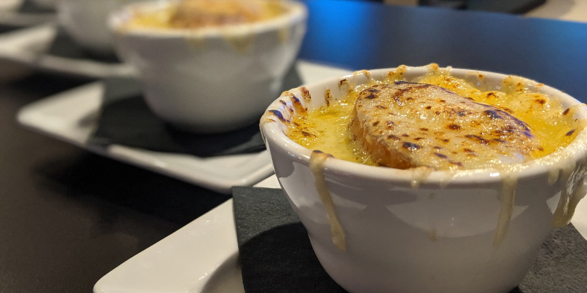 Three white ramekins filled with French onion soup sit on black napkins and white plates at Spare Time Texas. Each bowl is topped with toasted bread and melted cheese, with some cheese spilling over the sides. The focus is on the nearest bowl, adding a touch of warmth to your family fun center experience.