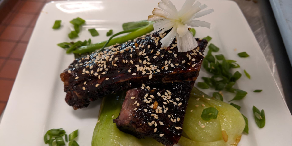 At Spare Time Texas, indulge in a dish of glazed pork ribs garnished with sesame seeds and a delicate white flower atop, served on a bed of bok choy. Scallions add flair while you enjoy the family fun center's vibrant atmosphere—perfect for dinner before hitting the bowling lanes.