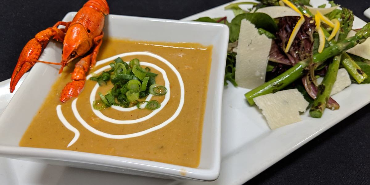 A creamy orange soup garnished with a swirl of cream, sliced green onions, and a small lobster takes center stage. Beside it is a fresh salad with mixed greens, shaved parmesan, and asparagus on a white plate—perfect for enjoying after a lively day at Spare Time Texas.