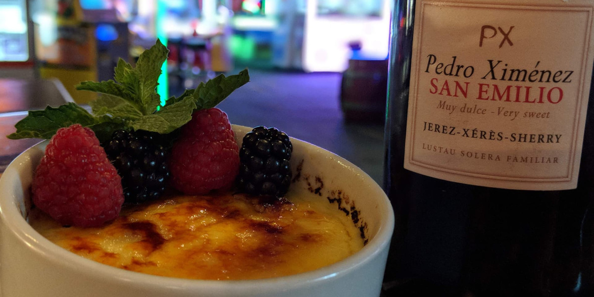 A creamy dessert topped with raspberries, blackberries, and mint leaves sits next to a bottle of Pedro Ximénez San Emilio sherry in a cozy corner of Spare Time Texas. This family fun center transforms into a dimly lit retreat for relaxation after the excitement of bowling.
